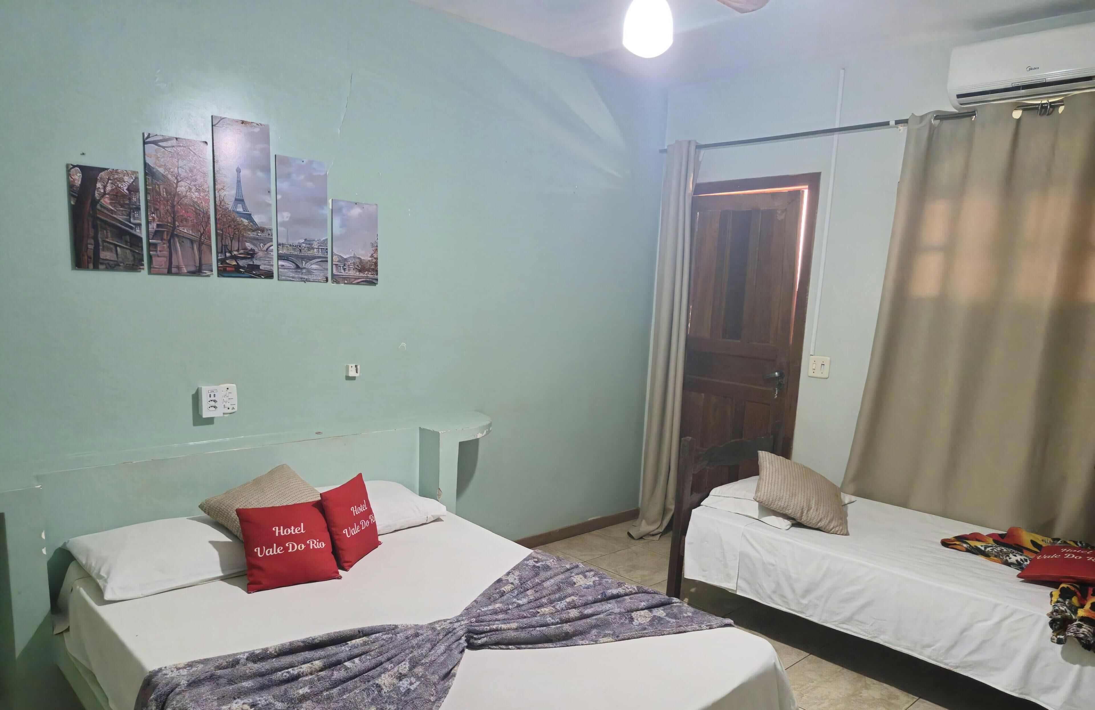A room with two beds, a headboard, a wall-mounted air conditioner, and a door with curtains.