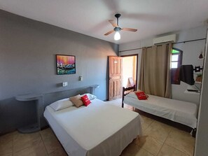 A hotel room with two beds, a ceiling fan, a painting, a desk, and a window with curtains.