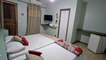 A hotel room with two beds, a desk with a TV, a small fridge, and a window with curtains.