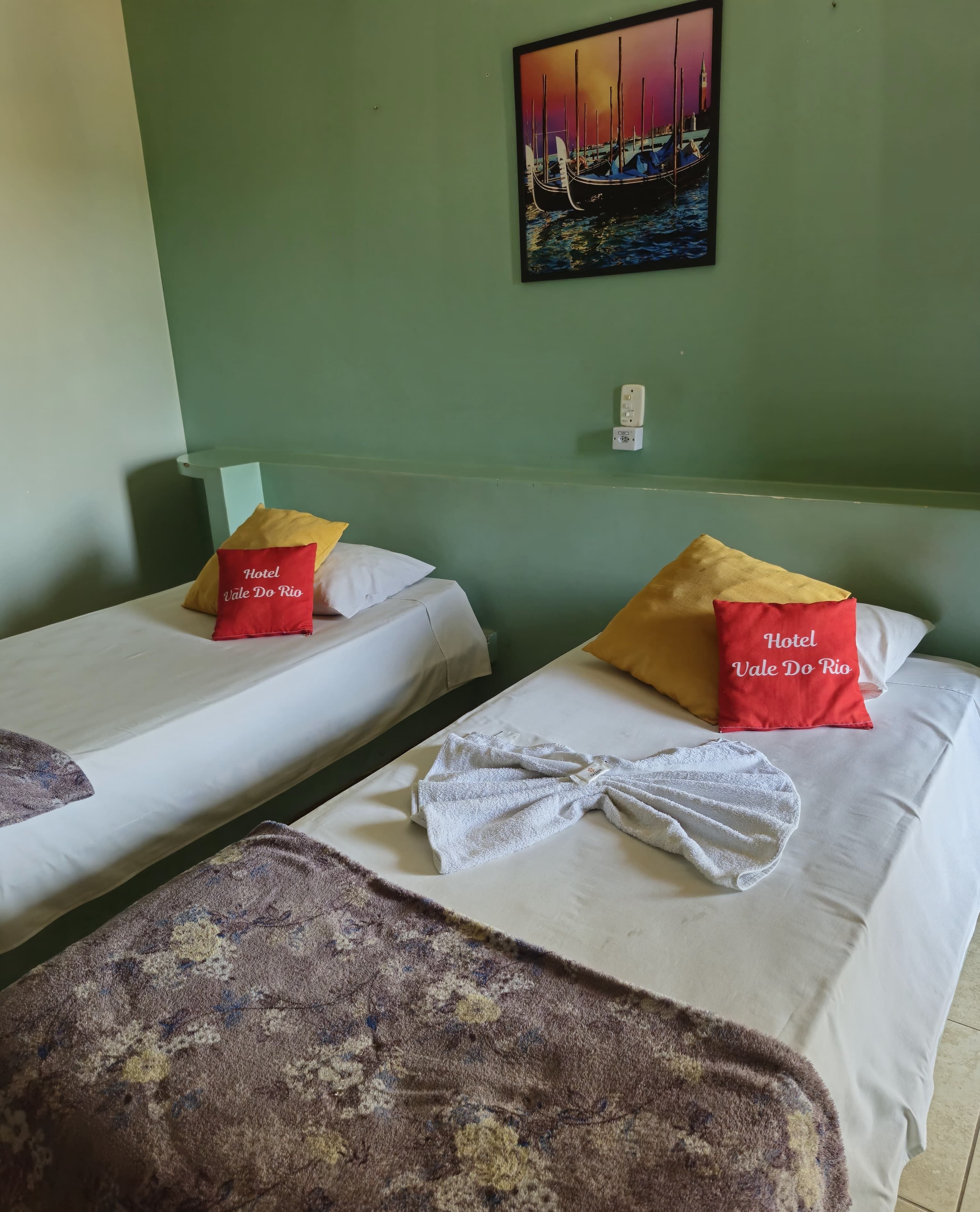 Ein Hotelzimmer mit zwei Betten, jedes mit einem Kissen mit der Aufschrift 'Hotel Vale Do Rio'.