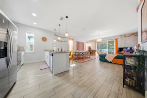 A modern kitchen with a central island, stainless steel appliances, and a dining area with a striped curtain. - Casita Coco - Private Pool - Foosball - BBQ (Kissimmee)