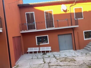 A courtyard with a stone floor, a grey door, and a white bench. - Holiday Home 'Il Focolare dei Sibillini' with Mountain View, Balcony & Wi-Fi (Fematre)