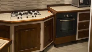 Eine Küche mit Gasherd, Backofen, Mikrowelle, Holzschränken und einer Uhr an der Wand.
