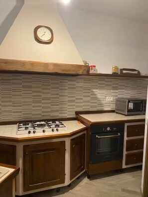 Eine Küche mit Gasherd, Backofen, Mikrowelle, Holzschränken und einer Uhr an der Wand.