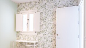 Ein Zimmer mit einem weißen Schreibtisch, einem kleinen Hocker und einem Kleiderschrank.