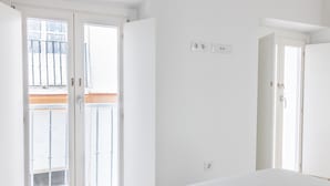 Ein heller, weißer Raum mit einem Bett, einem Fenster und einer Tür.