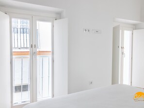 Une pièce lumineuse et blanche, avec un lit, une fenêtre et une porte.