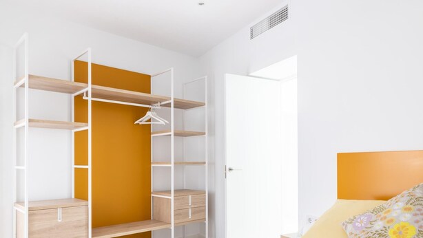 Ein Schlafzimmer mit einem Bett, einem Kleiderschrank mit mehreren Regalen und einer Tür zu einem anderen Raum.
