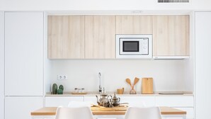 Eine moderne Küche mit weißen Schränken, einer Mikrowelle, einem Spülbecken und zwei weißen Stühlen an einem Holztisch.