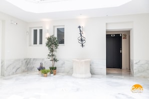 A modern lobby with marble flooring, potted plants, a decorative wall piece, and a door with a 'No Smoking' sign. - Apartamento Villalobos 6 by C diz Time Apartments (Cádiz)