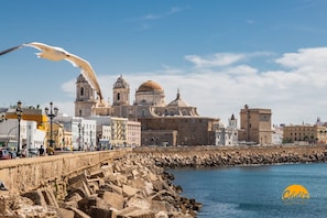 A coastal cityscape with historic architecture, a stone seawall, and a clear blue sky. - Apartamento Villalobos 6 by C diz Time Apartments (Cádiz)