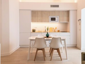 A modern kitchen with white cabinetry, a built-in microwave, and a dining area with white chairs and a wooden table. - Apartamento Villalobos 5 by C diz Time Apartments (Cádiz)