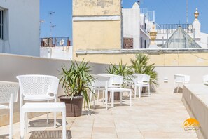 A rooftop terrace with white plastic chairs and tables, potted plants, and a view of buildings in the background. - Apartamento Villalobos 2 by C diz Time Apartments (Cádiz)