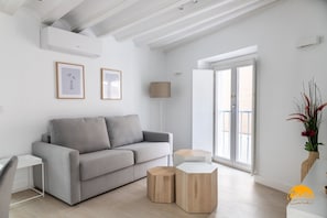 A modern living room with a grey sofa, wooden side tables, and a large window with a view. - Apartamento Villalobos 3 by C diz Time Apartments (Cádiz)