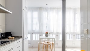 A modern kitchen with white cabinetry, a granite countertop, and a dining area with a white table and four chairs. - Green Home by Cadiz Time (Cádiz)