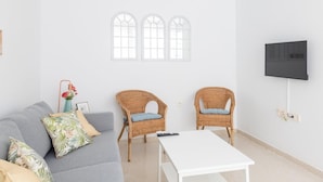 A living room with a grey sofa, two wicker chairs, a white coffee table, and a TV mounted on the wall. - Green Home by Cadiz Time (Cádiz)