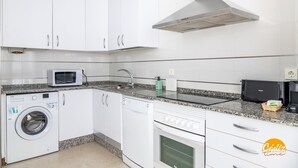 A modern kitchen with white cabinets, a built-in washing machine, a microwave, and a coffee maker. - Green Home by Cadiz Time (Cádiz)