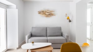 Ett modernt vardagsrum med en grå soffa, ett vitt soffbord och en gul stol. En fiskdekoration som hänger på väggen syns.