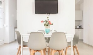 A dining area with a white table, grey chairs, and a vase with flowers. - Apartamento Floral by Livework (Cádiz)