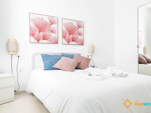 Ein Hotelzimmer mit einem weißen Bett, zwei Kissen, einem weißen Nachttisch, einem Spiegel und zwei Wandlampen.