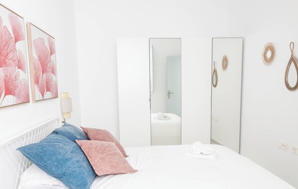 A hotel room with a bed, pillows, a bedside table, a mirror, and a wall-mounted light fixture. - Apartamento Floral by Livework (Cádiz)