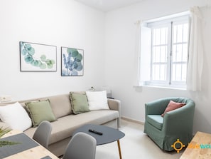 A modern living room with a sofa, a green armchair, a small round table, and two framed botanical prints on the wall. - Estudio Palma by Livework (Cádiz)