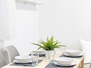 A dining table set with white plates, bowls, and glasses, accompanied by a potted fern. - Estudio Palma by Livework (Cádiz)