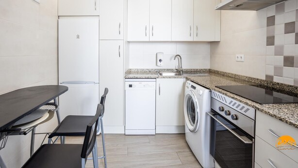 A compact kitchen with white cabinets, a built-in dishwasher, a washing machine, and a stove. - Atico Catedral by Cadiz Time (Cádiz)