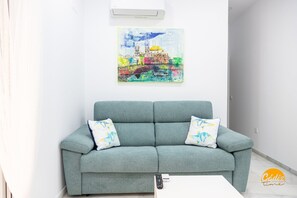 A living room with a grey sofa, two patterned cushions, a white coffee table, and a colorful painting on the wall. - Casa Patio La Vi a by Cadiz Time (Cádiz)