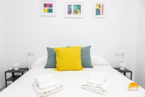 A neatly made bed with white linens, a bright yellow pillow, and teal pillows. There are three framed artworks on the wall above the bed. - Casa Patio La Vi a by Cadiz Time (Cádiz)