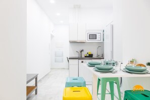 A modern kitchen with white cabinets, a microwave, and a sink. There are stools and a bench in the dining area. - Casa Patio La Vi a by Cadiz Time (Cádiz)