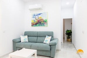 Een woonkamer met een grijze bank, een witte salontafel en een kleurrijk abstract schilderij aan de muur.