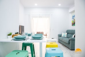 Een moderne woonkamer met een eethoek, een bank en een kleurrijk schilderij aan de muur.