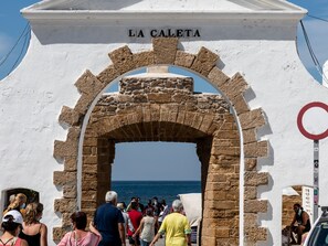 Ein Steinkunstwerk mit der Aufschrift „LA CALETTA“ darüber, das zu einer Küstenregion mit dort versammelten Menschen führt.