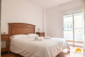 A bedroom with a wooden headboard, a large bed with white bedding, a nightstand with a lamp, and a view of the outside through a sliding glass door. - Villa Lola by Cadiz Time (Cádiz)