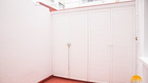 Un muro esterno bianco con pavimento in piastrelle rosse e una porta bianca con pannelli a persiana orizzontale.