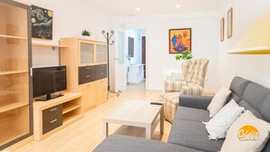 Un soggiorno moderno con divano, televisione e tavolino. Si nota una libreria e un mobile contenitore con una TV sopra.