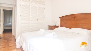 Una camera d'hotel con un letto grande, lenzuola bianche, una testiera in legno, un comodino con una lampada e un armadio con ante a listelli.