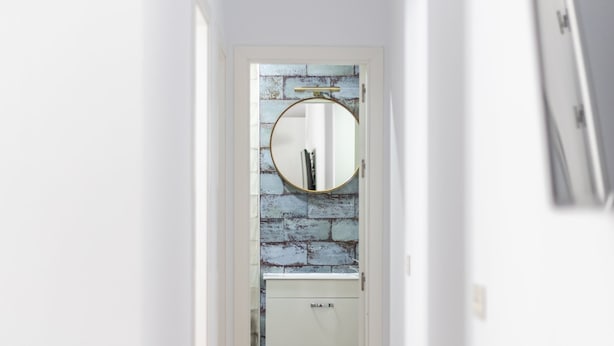 A narrow hallway with a white door at the end, a round mirror on the wall, and a white cabinet below. - El Patio del Mar by Cadiz Time (Cádiz)