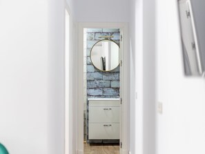 A narrow hallway with a white door at the end, a round mirror on the wall, and a white cabinet below. - El Patio del Mar by Cadiz Time (Cádiz)