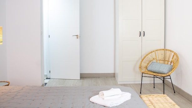 Ein Schlafzimmer mit einem Bett, einem Kleiderschrank, einem Korbsessel und einem kleinen Teppich.
