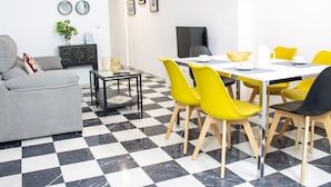 Ein Essbereich mit Schachbrettmuster-Boden, einem Tisch mit gelben Stühlen und einer modernen Küche im Hintergrund.