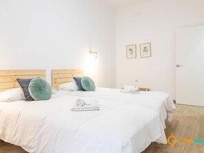 A hotel room with a wooden headboard, white bedding, two green pillows, a rolled white towel, and two framed pictures on the wall. - Casa del Pescador by Livework (Cádiz)