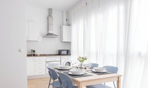 A modern kitchen with white cabinets, a microwave, and a stove. There is a dining table set with plates, glasses, and a vase of flowers. - Casa del Pescador by Livework (Cádiz)