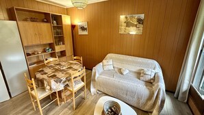 Ein gemütlicher Raum mit einer holzgetäfelten Wand, einem Esstisch mit Stühlen, einer Couch und einem kleinen weißen Tisch mit einem Korb.