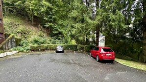 Ein Parkplatz mit zwei Autos, umgeben von Bäumen und einer Backsteinmauer.