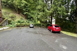 A parking area with two cars, surrounded by trees and a brick wall. - Alpine refuge near the forest road (Mont-Dore)