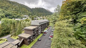 Eine mehrgeschossige Parkgarage neben einem Gebäude mit flachem Dach, umgeben von üppiger Vegetation und einer Bergkulisse.
