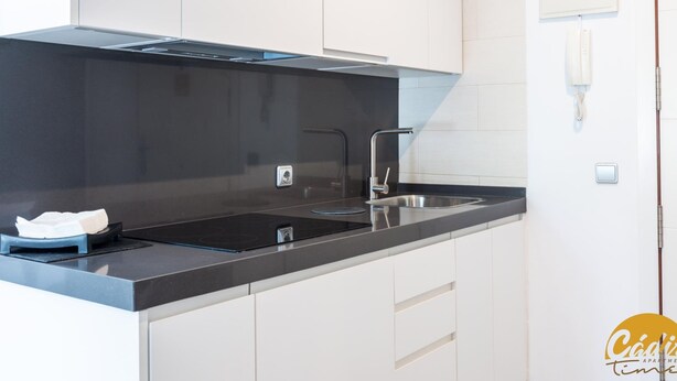 A modern kitchen with a black countertop, stainless steel sink, and white cabinets. - Apartamento Plaza Mina by Cadiz Time (Cádiz)