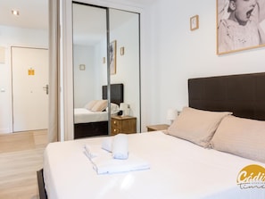 A hotel room with a bed, a bedside table, a nightstand, a mirror, and a door. - Apartamento Plaza Mina by Cadiz Time (Cádiz)